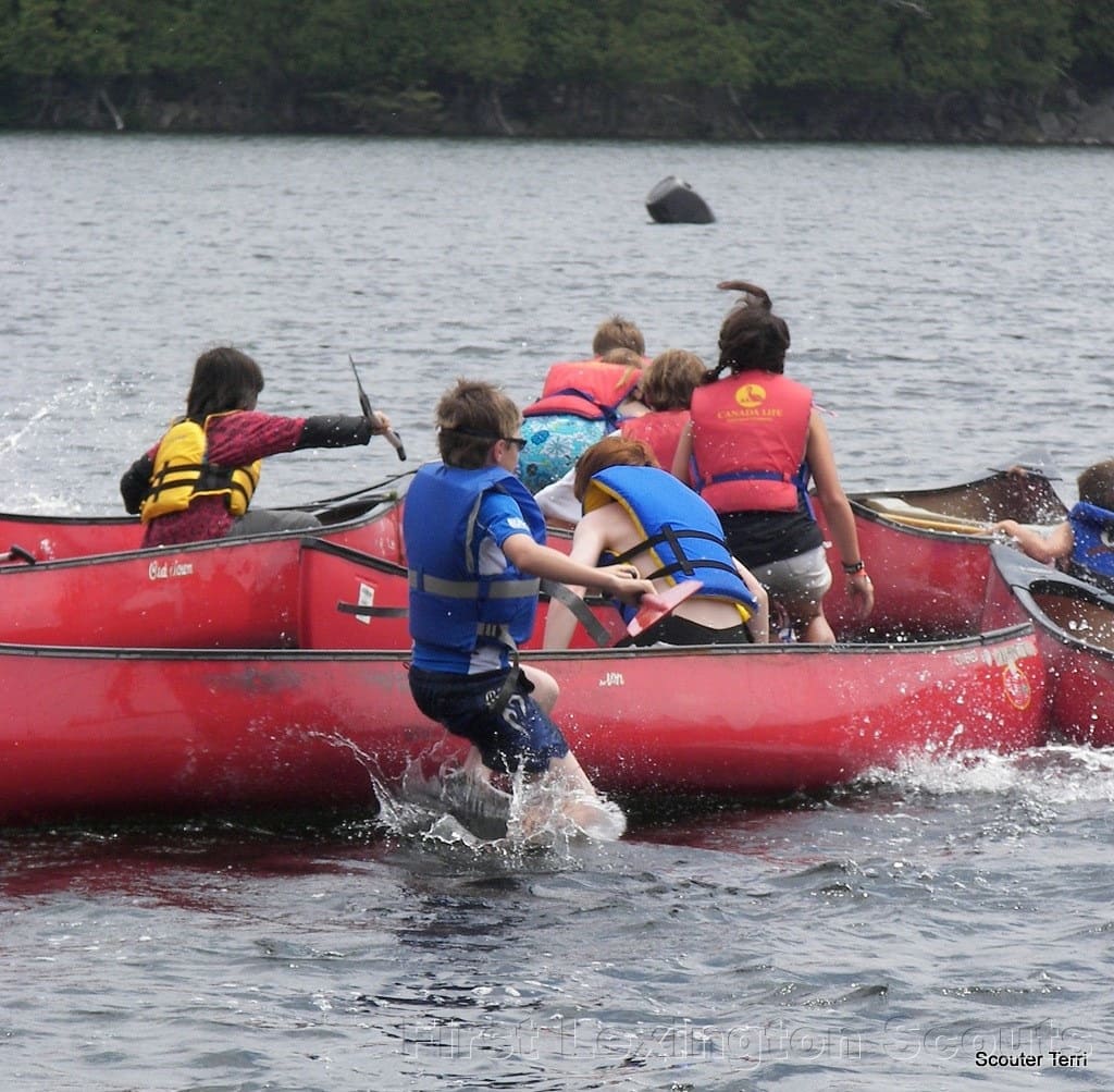 Scouts jumping into red canoes for start of a canoe race