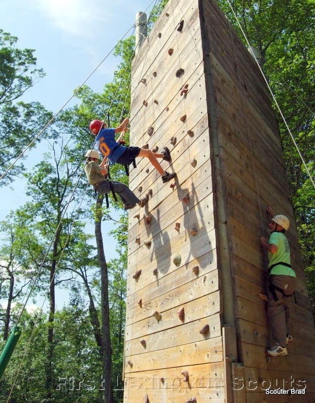 3 Scouts climbing tall wooden climbing wall with hand and foot holds embedded